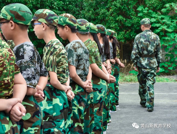 双手背在后面,右手握拳,左手握住右手手腕,教官细心地教授着"跨立"