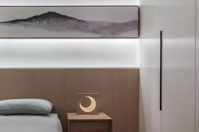 次卧木饰面的床头,一幅中式画加灯带洗墙的设计,月牙台灯,清雅的床品