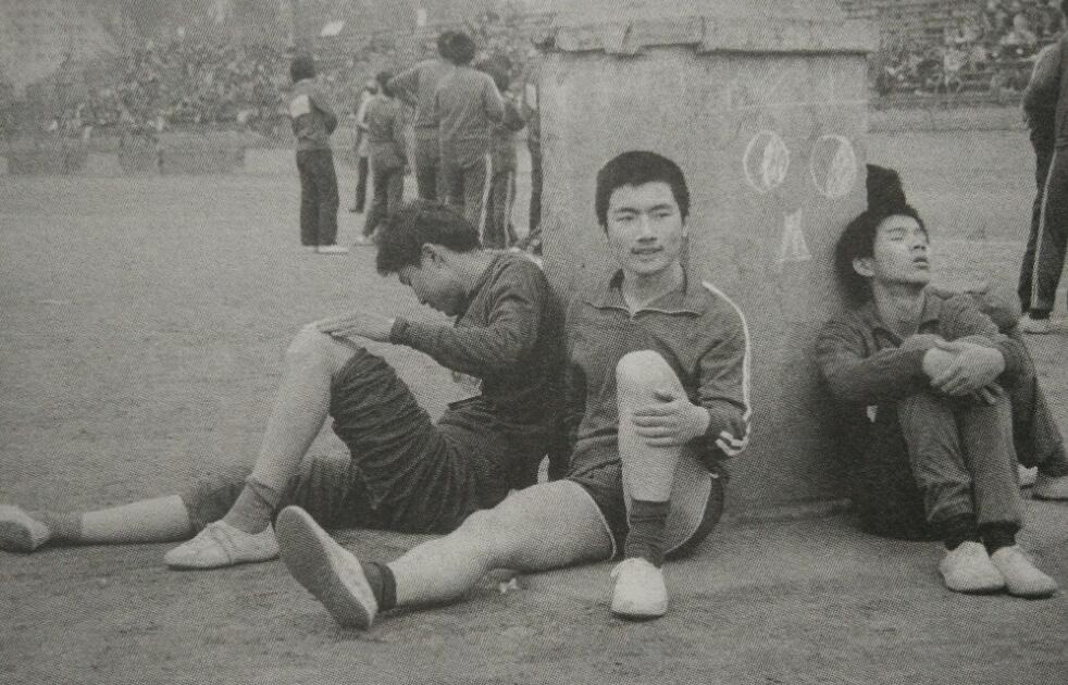 80年代学生历史老照片:学校开运动会,几个男同学靠在操场的一个柱子上