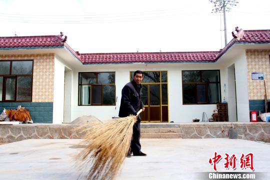 图为民和县松树乡牙合村贫困户李长生在搬迁新村打扫新家园.