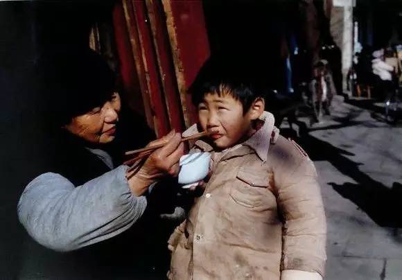 扬州街头,正在给孙子喂饭的奶奶,孙子一脸厌恶的表情.