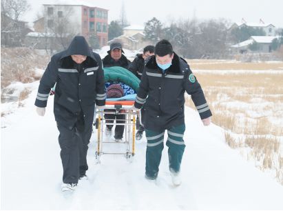 1月27日,医务人员和家属在风雪中竭力推动救护车担架.