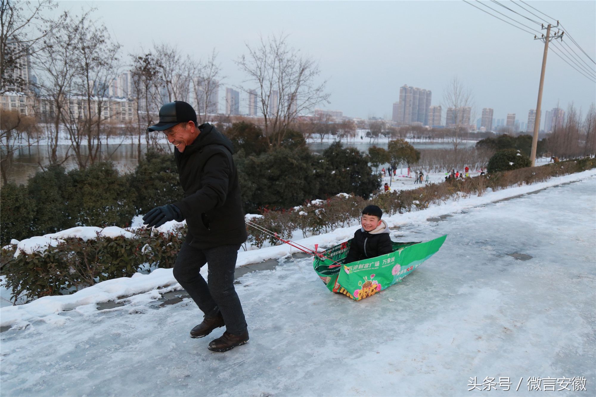 图为1月29日,滑雪结束后,一名儿童坐在自制的滑雪袋上,让爷爷拉着回家
