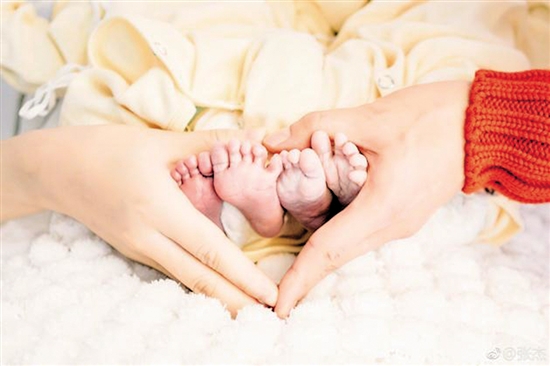 照片中,夫妻俩用手围成爱心,轻轻握住两个宝贝的小脚,温柔爱意满溢.