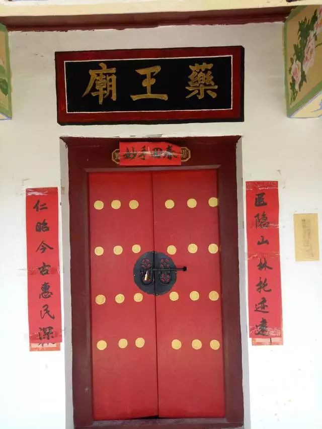 繁体大字"药王庙,大红铁门上挂着一把风格别致的插销,还贴着一副对联