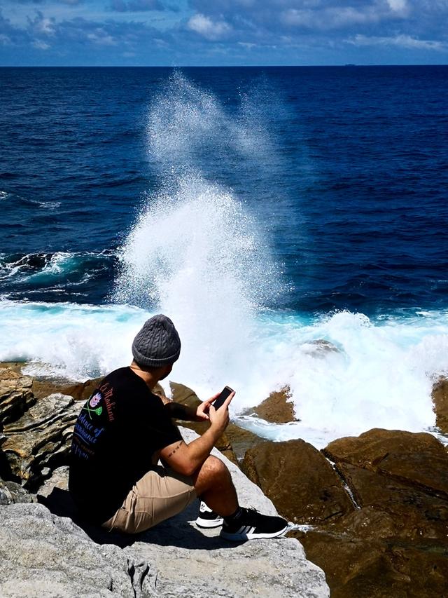 海边岩石上玩手机的淡定哥