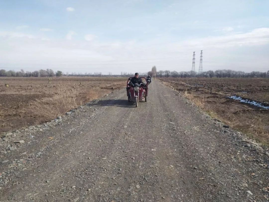 村民驾驶着三轮摩托车行驶在平坦的砂石路上