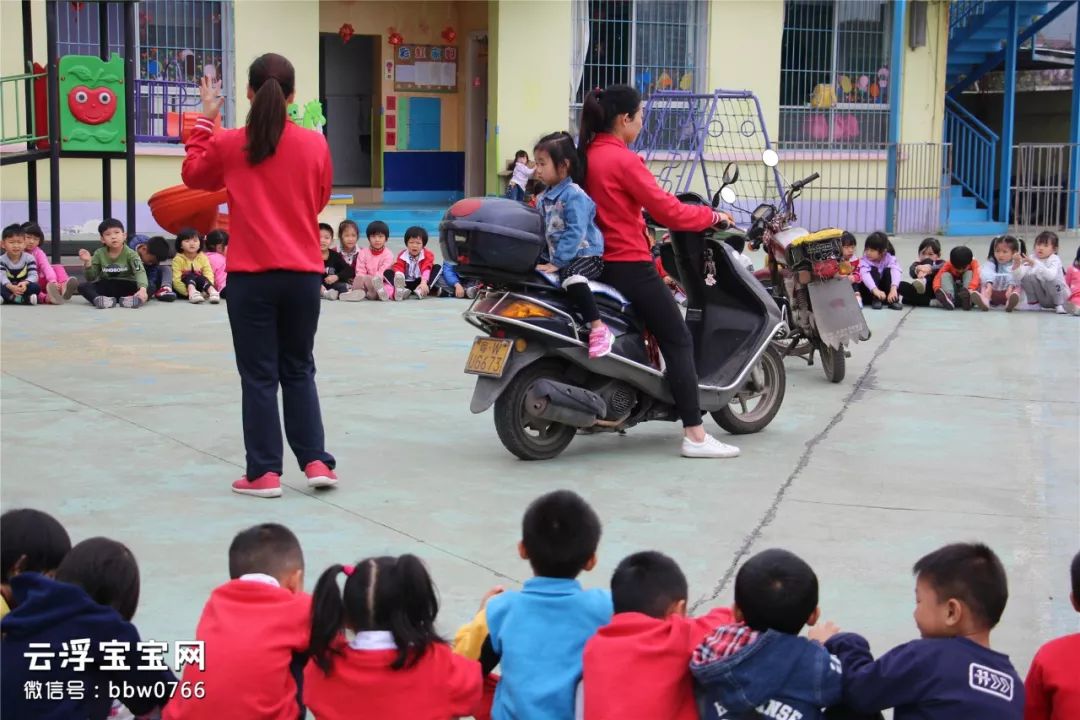 幼儿园操场中间停了2辆摩托车,老师和孩子们在