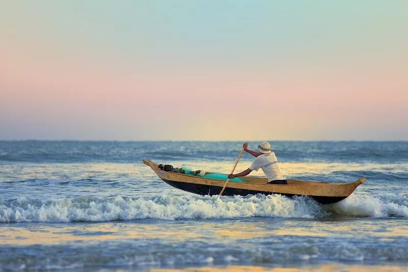 海岸边的渔民驾着小船出海,很快就淹没在浪涛的后面.