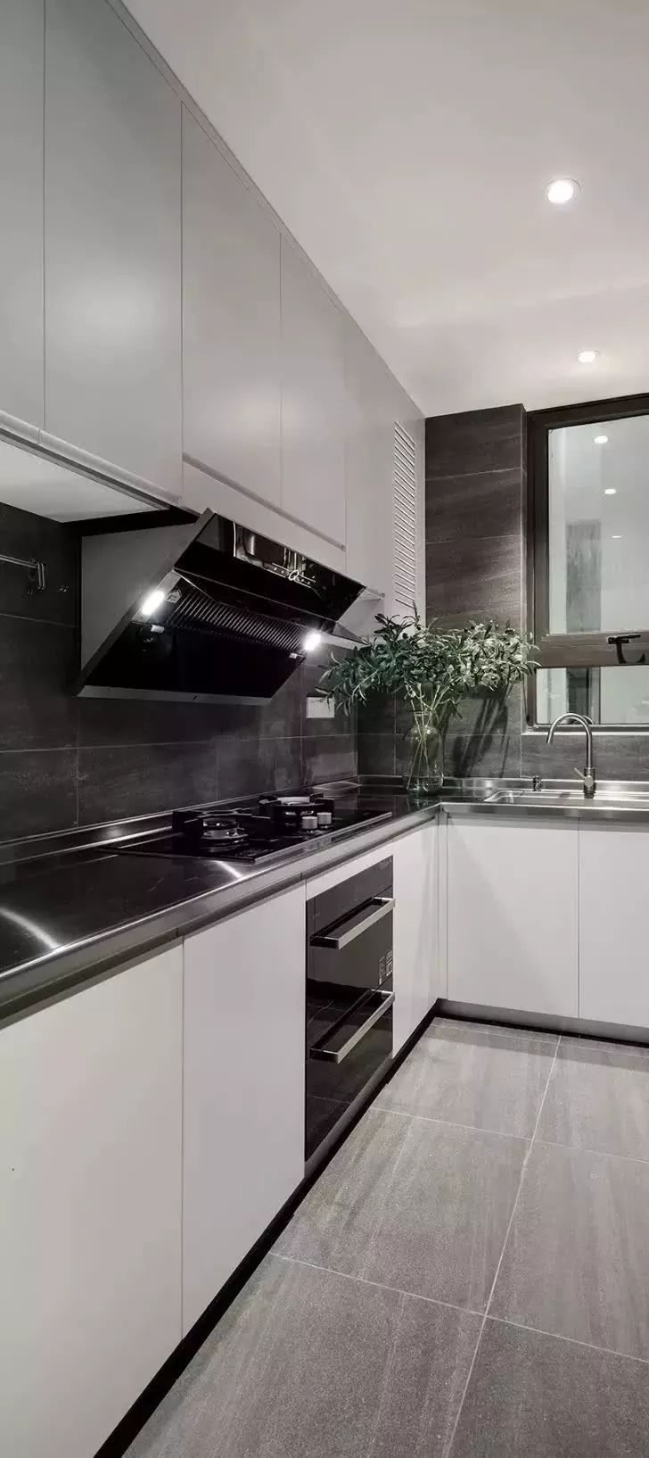 厨房的深灰色墙面 浅灰色地面 不锈钢台面 白色柜体,既给人时尚的感觉