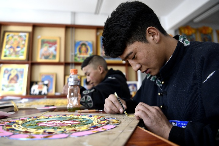 海南藏族自治州职业技术学校17级唐卡班学生尕藏多杰(右)在课堂上制作