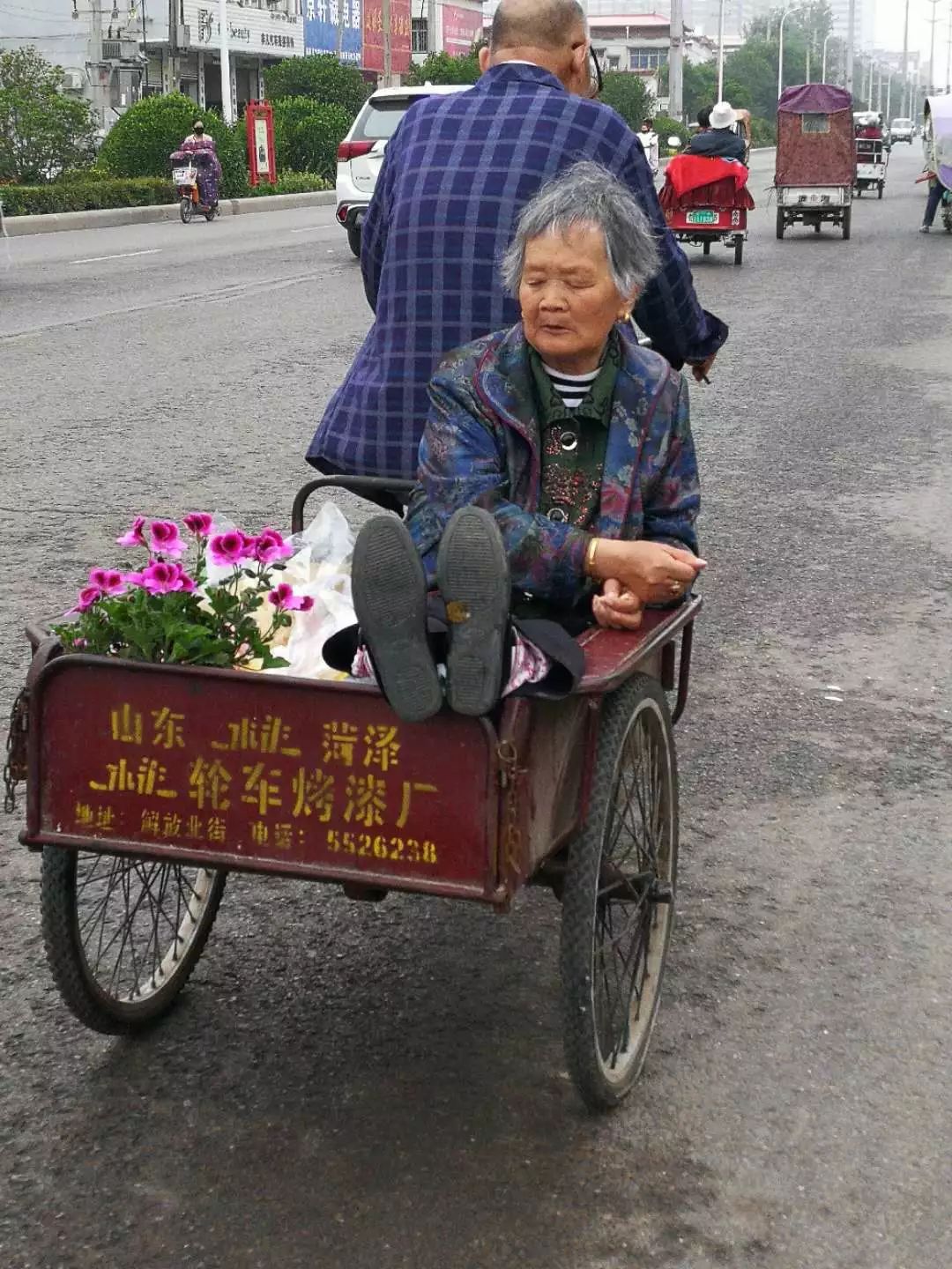 5月18日上午,老大爷骑着三轮车载着老太太,三轮车上放着刚刚从市场买