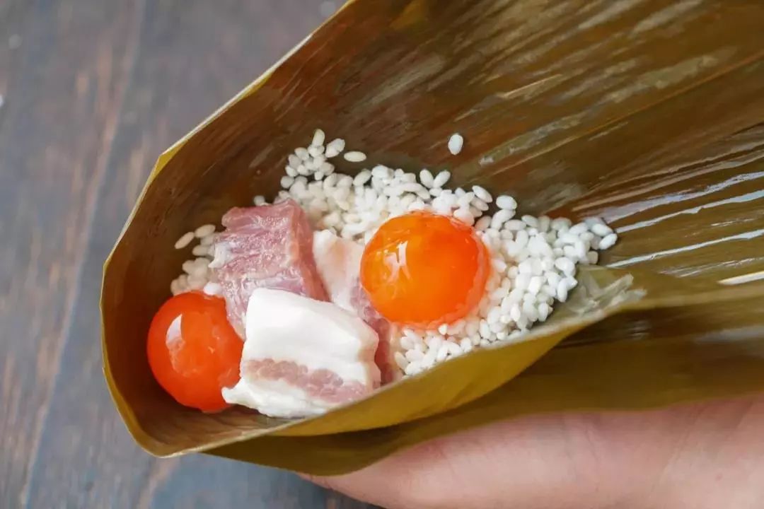 3,每只粽子先填入一半的糯米,然后放入1块五花肉,1颗咸蛋黄,再将