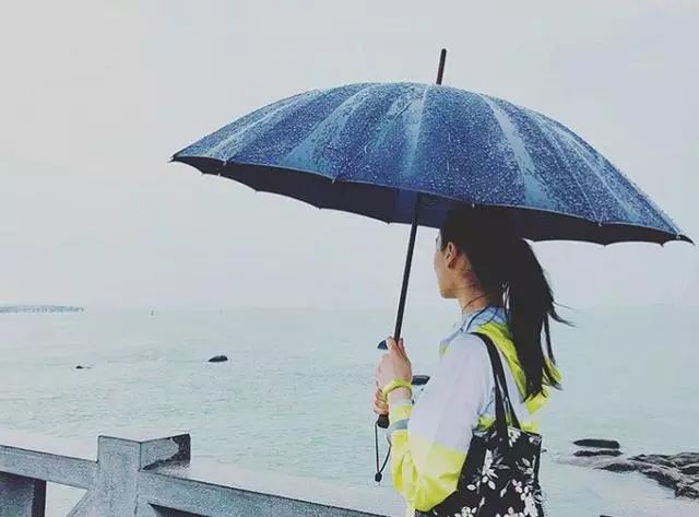 照片中她没有露出正脸,而是背向镜头,举伞在雨中漫步