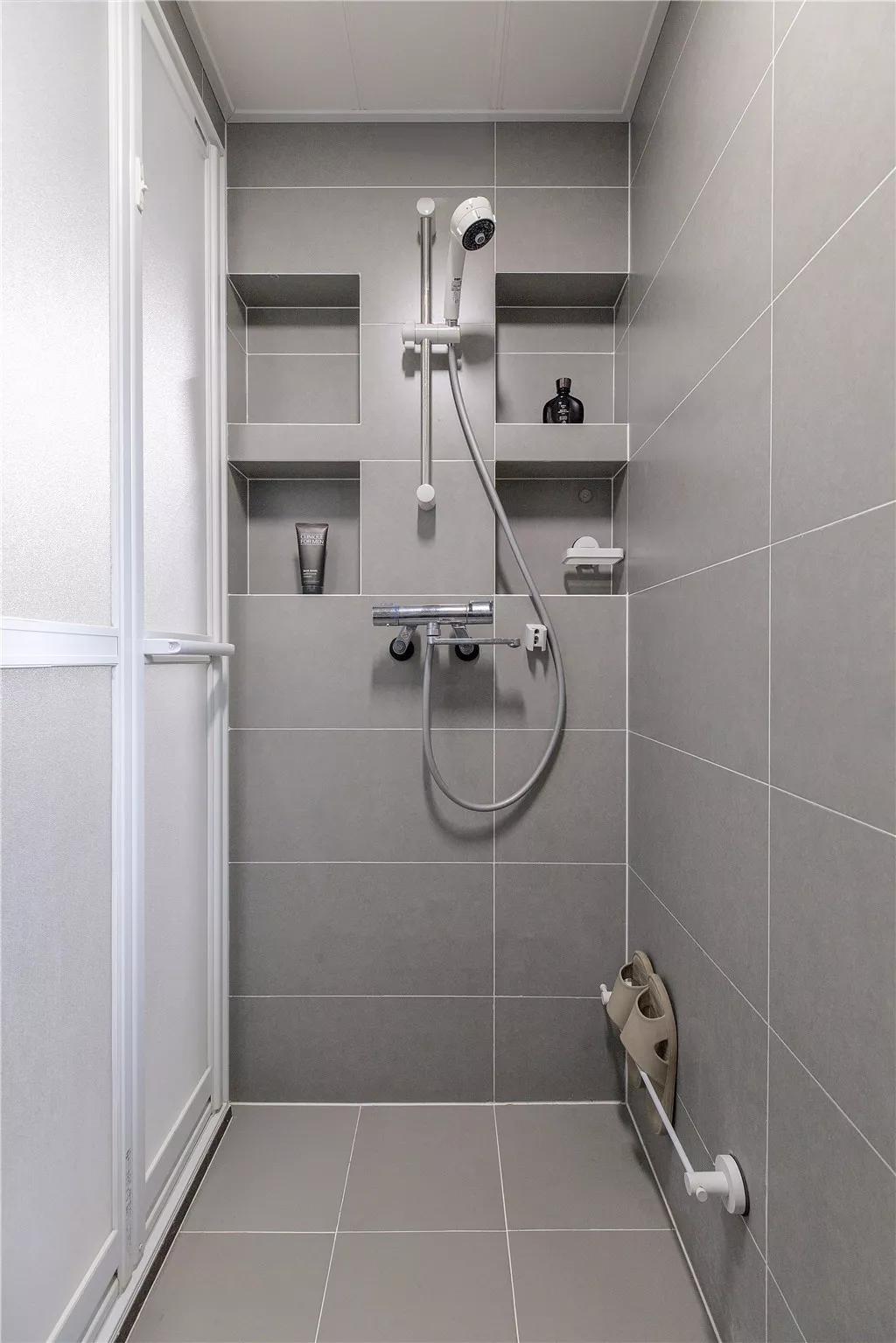 淋浴房墙地面铺设灰色亚光砖,在淋浴花洒的两侧都做了壁龛收纳,用于