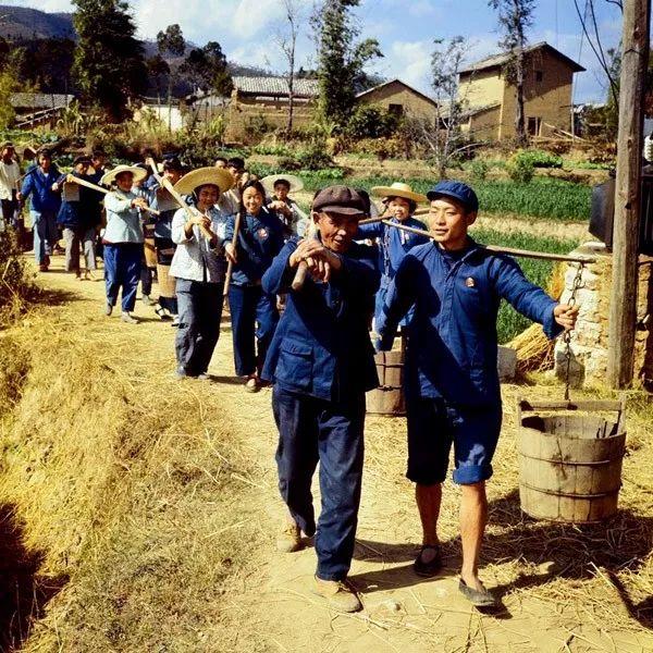 1970年,云南峨山彝族自治县,知识青年与农民一起挑着担子,扛着锄头下