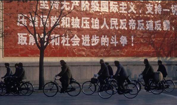 骑自行车的人们经过贴着醒目标语的墙.