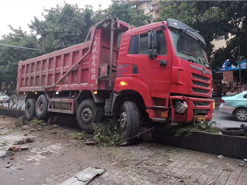 一辆大货车 开着应急灯"骑"在残留的绿化带上 被撞变形 右前方保险杠