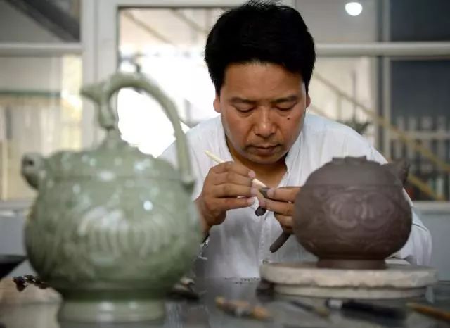 崔涛在对手工制作的耀州窑青釉剔花倒装壶进行修坯(7月10日摄).