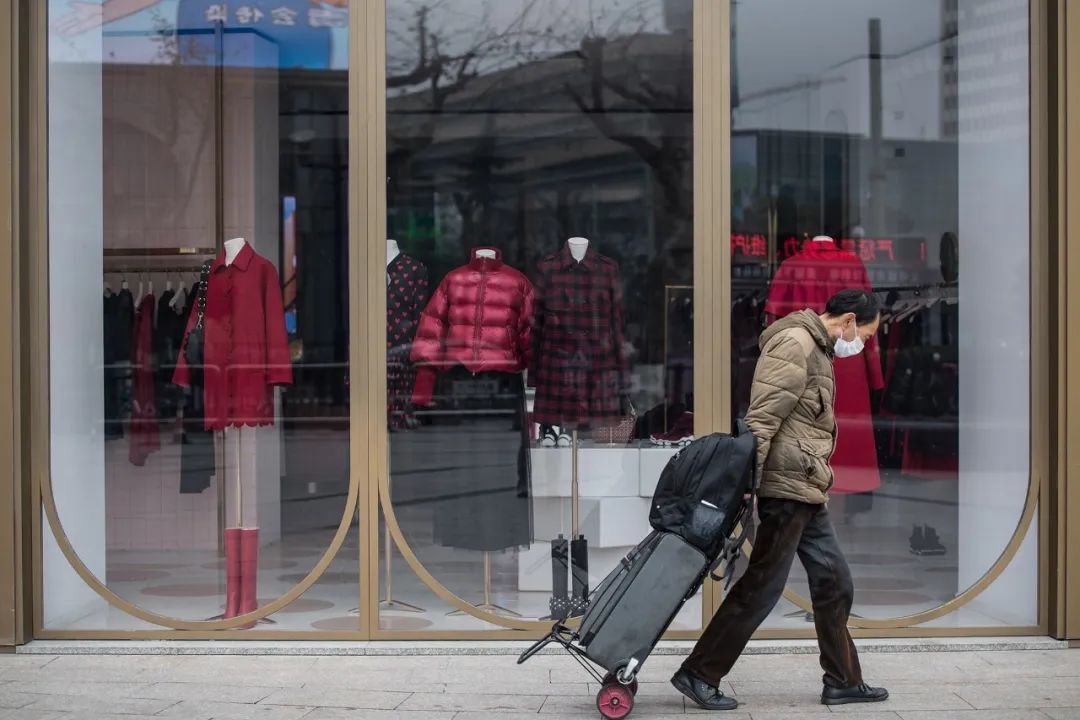 2月8日,国大城市广场附近,一位行人拖着行李路过商场橱窗,看起来稍显