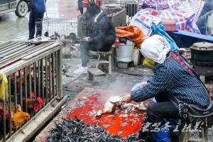 从江西山集市上一位大嫂在鸡笼边杀鸡拔毛,鸡们还好奇地伸着头看