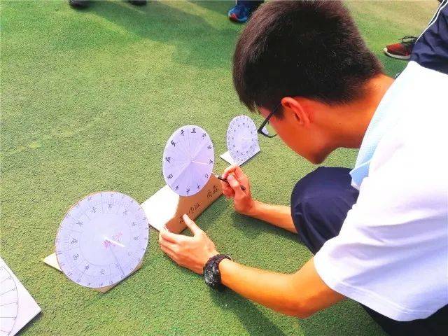 阳光明媚,几十个小小的手工日晷在绿色塑胶地面上一字摆开,孩子们有