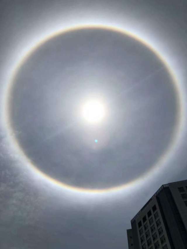 圆形的绚烂光环环绕太阳,浮现城市上空,如彩绸当空舞动,自然光景,触动