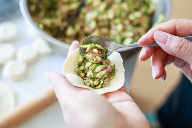 把调好的饺子馅摊放在饺子皮中间位置,捏成饺子.