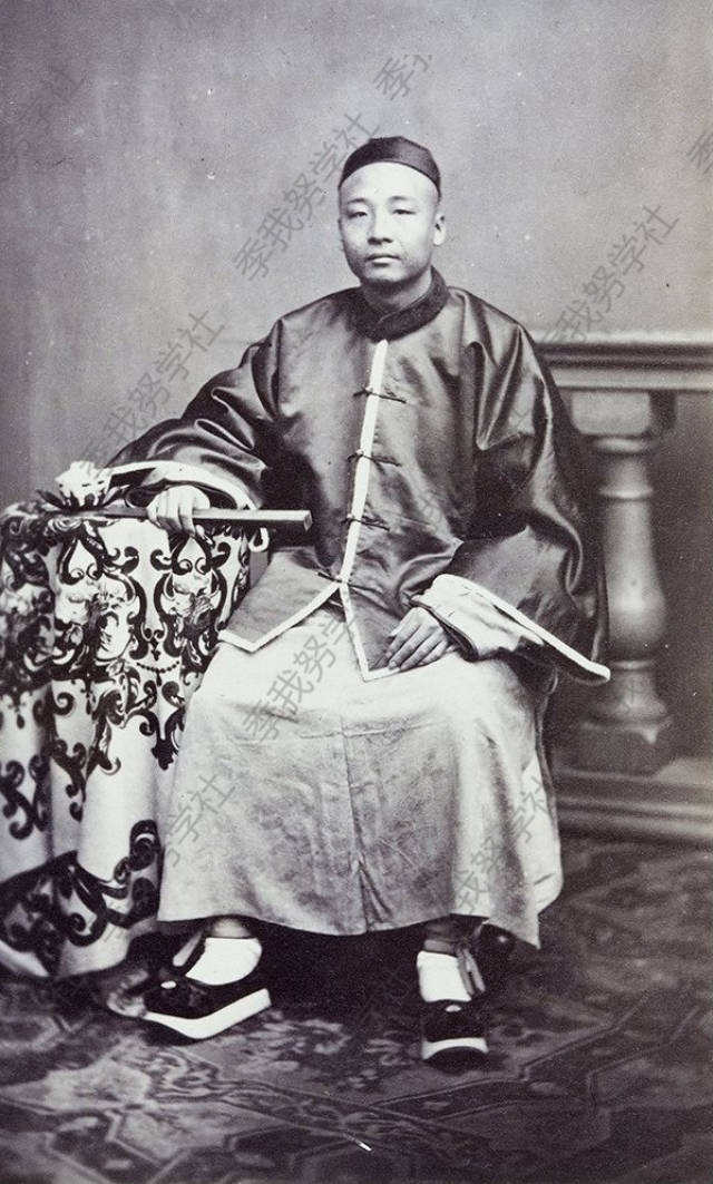 1870-1875年,一个中国男性.身穿传统中式马褂,戴着瓜皮帽,手执折扇.