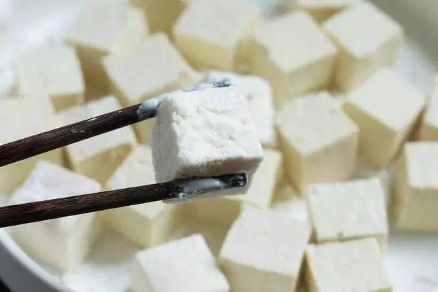 4,将切好的豆腐块均匀裹上淀粉,锅内倒油加热,放入老豆腐块,煎至表皮