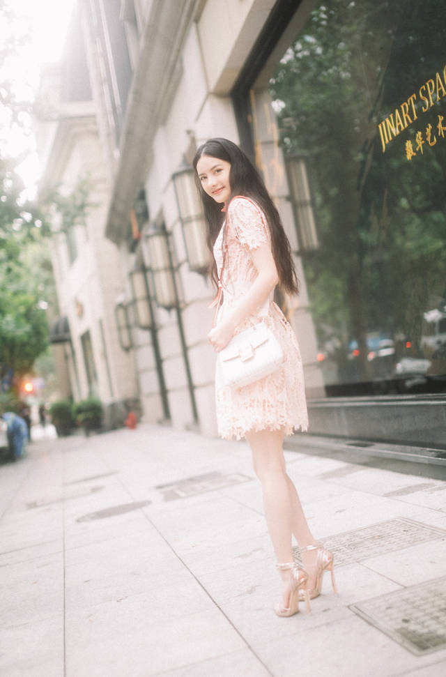 照片中,张芷溪身穿粉色镂空连衣裙,搭配金色透明高跟鞋,红白相间的
