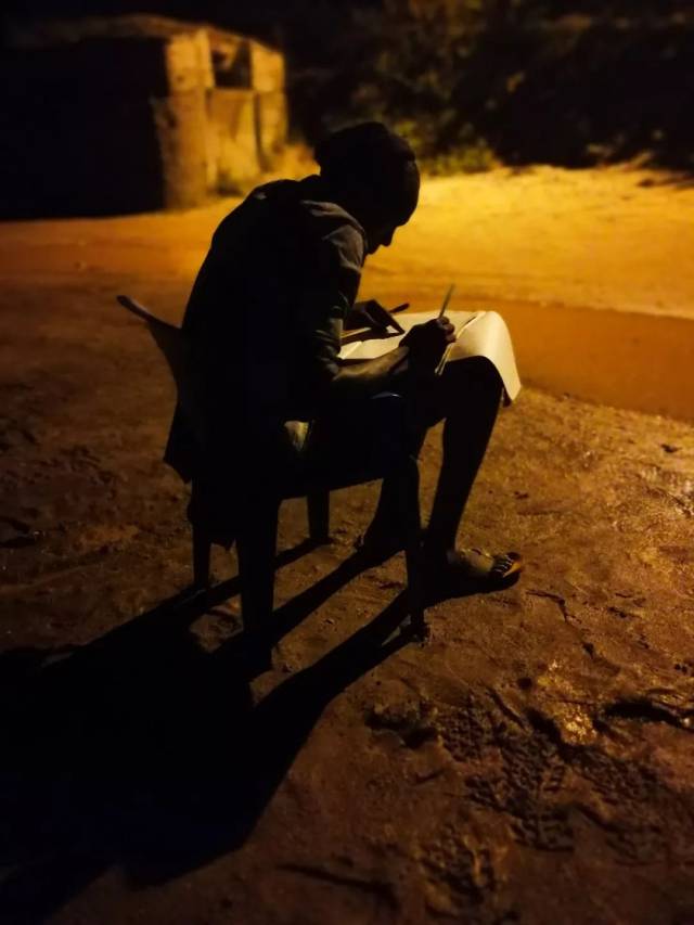 由于难民营里没有电力供应,这个孩子只能借助围墙的路灯看书学习.