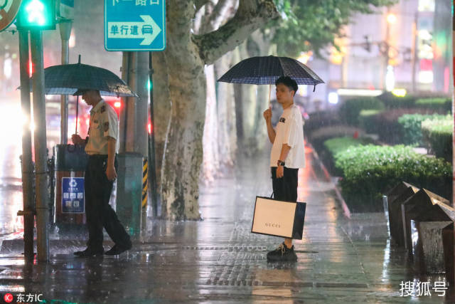 刚逛完街的男子在雨中撑伞等待过红绿灯.