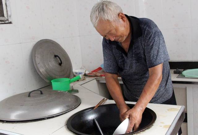 图为老人正在老伴和孙子们做饭.