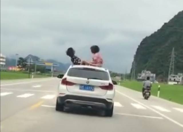 从两名女子被风吹卷的头发来看,车速较快,二人坐在车顶还做出身体后仰