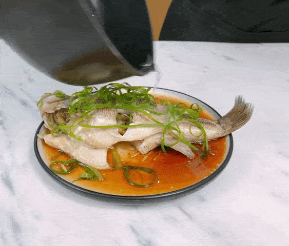 择去鱼身上的姜丝葱段,把用水泡好的葱花放在上面,锅内烧热油淋在鱼