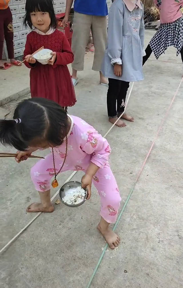 从画面中看到一个小女孩正端着碗筷跳皮筋,而且这个小女孩是光着脚丫