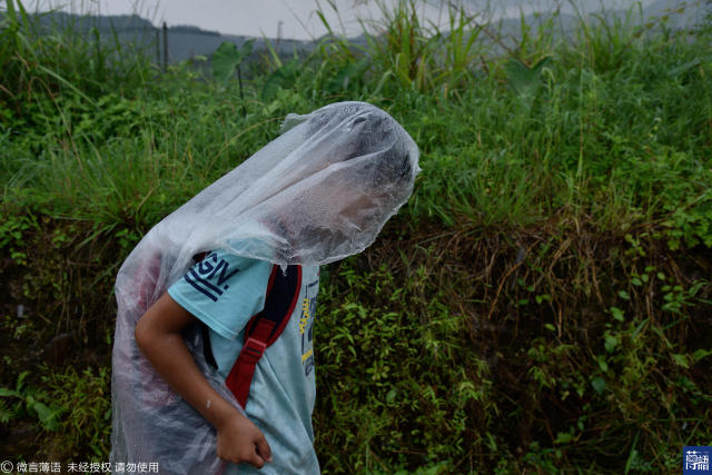 孩子身上的衣服已经被雨水淋湿,他却紧紧的用塑料布护着书包.