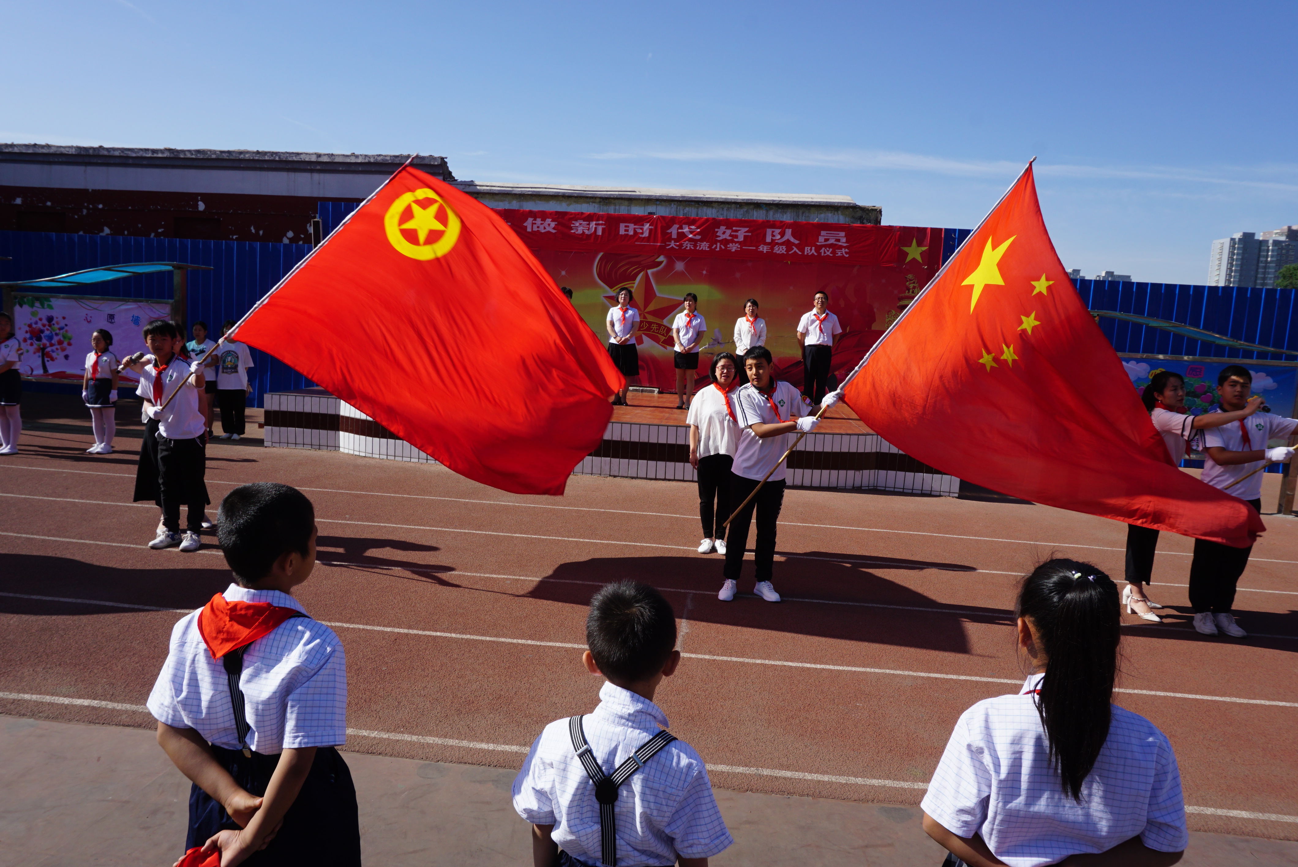 学校四位教师分别将党旗,国旗,团旗,队旗授于少先队员手中,四面红色