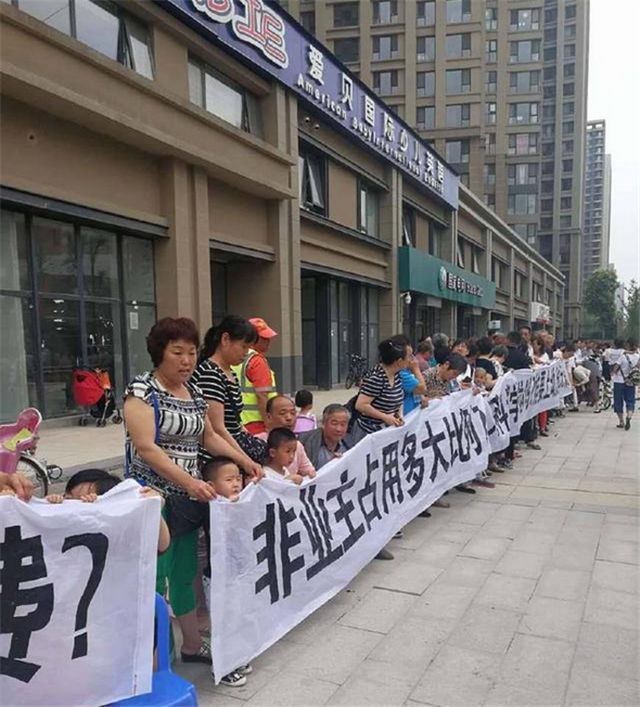 业主们手里的横幅上讽刺地写到:一女嫁八男,万科城学校到底承诺了多少