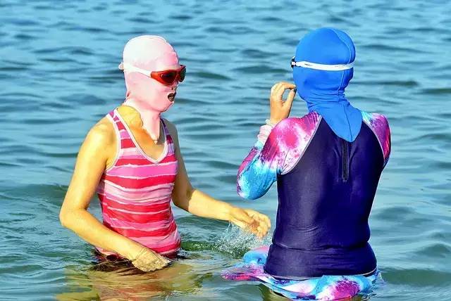 风靡青岛海滩,众多中老年妇女头戴五彩缤纷的脸基尼下海游泳健身,成为