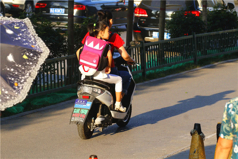 骑着电动车送孩子上学,孩子依偎在大人怀里.