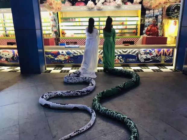 图中两位女子做白蛇与青蛇的打扮,撑伞现身商场,尾巴拖在地上,十分