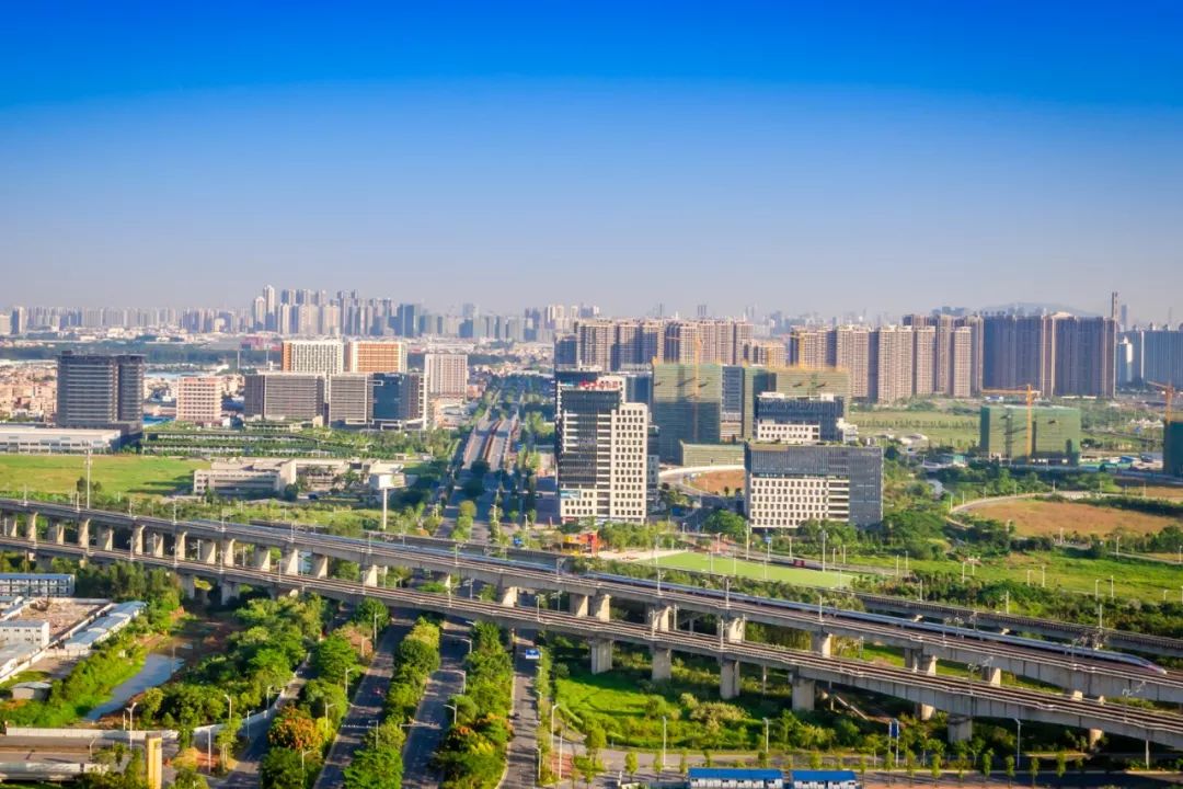 从空中俯瞰三龙湾三山新城片区,高楼林立,复兴号列车穿城而过,粤港
