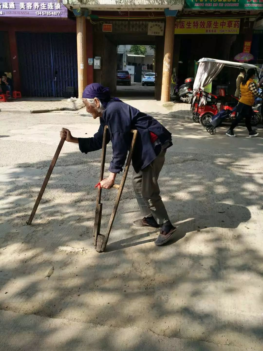 老奶奶一个人拄着两根拐杖缓慢地在路上艰难的行走着,真怕她一不小心