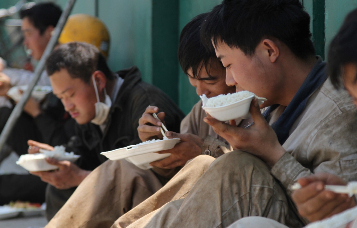 江苏启东,在船厂施工场地上,几位 农民工 席地而坐,吃着简单的盒饭