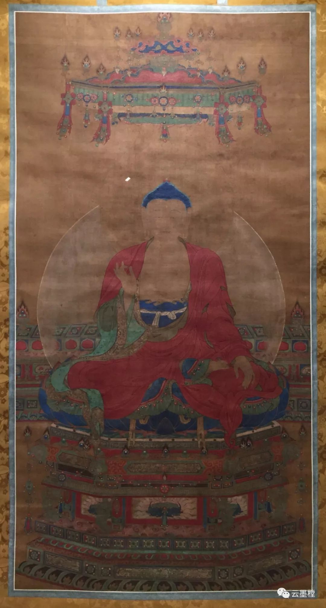 佛像结珈跌坐于莲花须座上,身着红色袈裟,双手结毗卢印举至胸前.