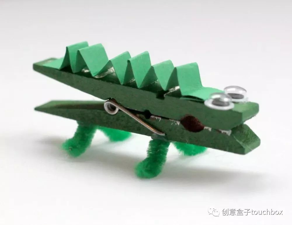 用绿色的扭扭棒扭出鳄鱼的双腿并粘贴在夹子下方用热胶枪将万能眼睛和