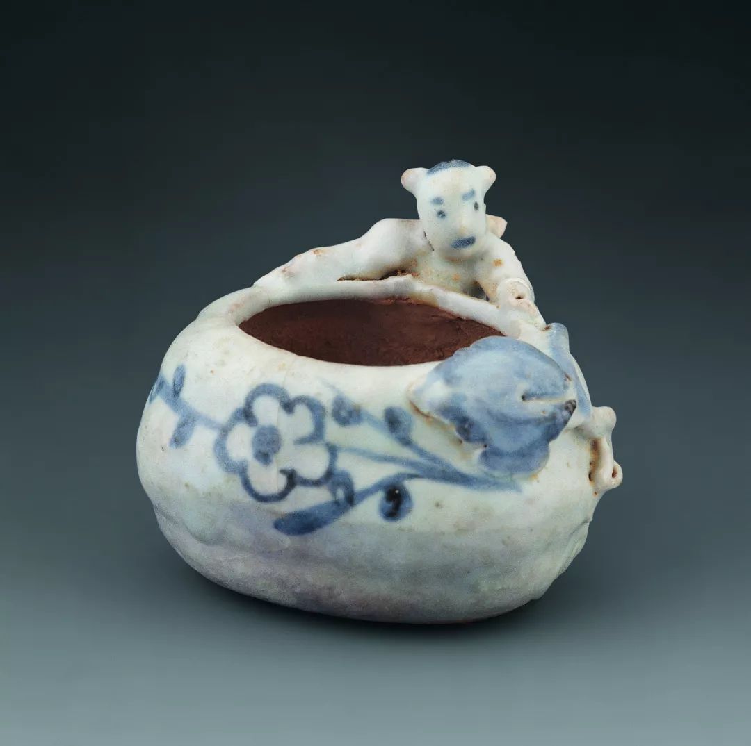 罐口沿处堆塑折枝桃,幼童扎双髻,俯于罐身之上,作抱罐状,纹饰简练