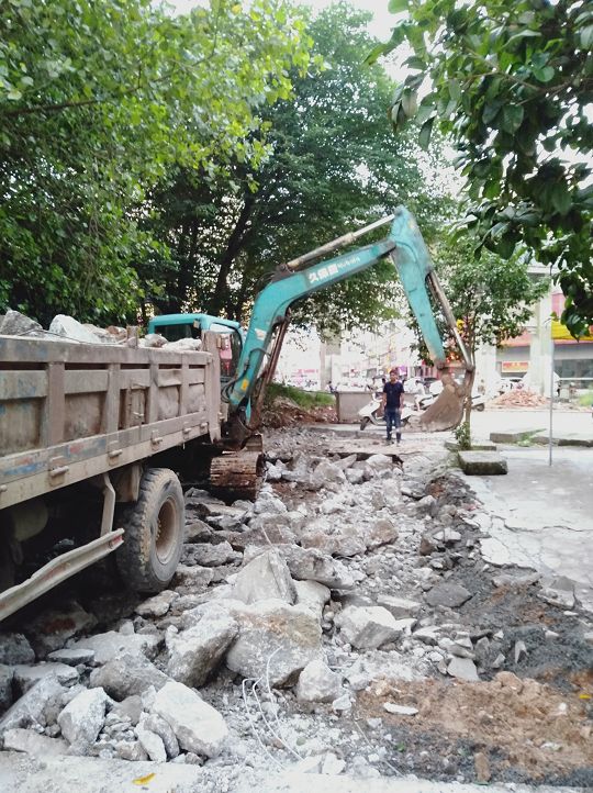 6月25日,一台挖掘机在京里街西门路口对破烂街面进行"清创"作业.